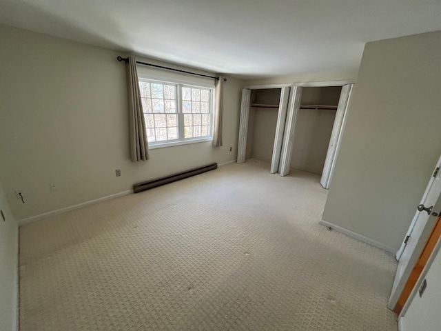 unfurnished bedroom featuring a baseboard radiator, two closets, light carpet, and baseboards