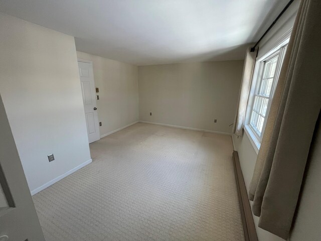 spare room with light carpet, baseboard heating, and baseboards