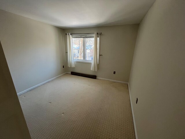 spare room with a baseboard heating unit, light carpet, and baseboards