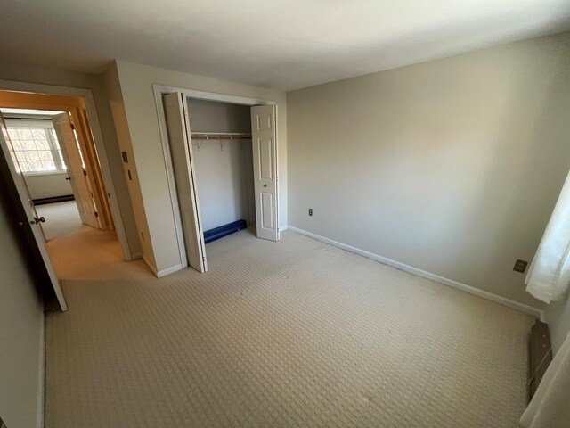 unfurnished bedroom with light carpet, a closet, and baseboards