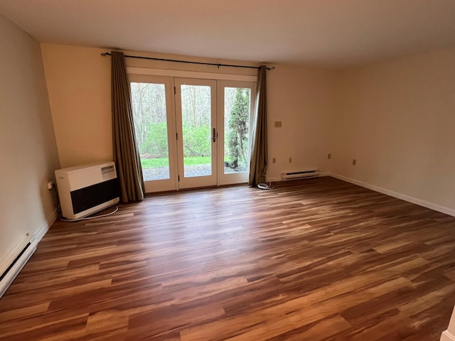spare room featuring baseboard heating, wood finished floors, baseboards, and heating unit