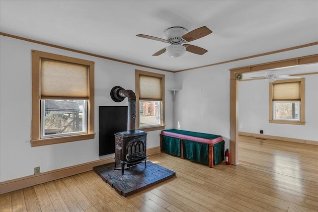 living area with a ceiling fan, a wood stove, healthy amount of natural light, ornamental molding, and hardwood / wood-style flooring