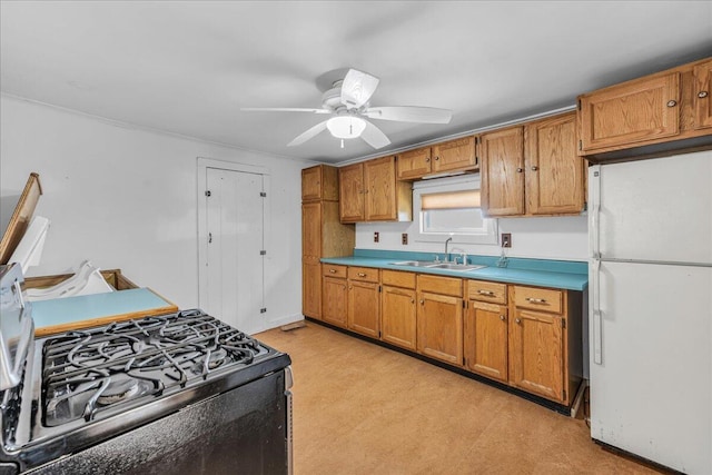 kitchen featuring freestanding refrigerator, a sink, black gas stove, ceiling fan, and brown cabinets