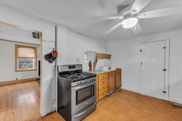 kitchen featuring stainless steel range with gas cooktop, light wood finished floors, a ceiling fan, brown cabinets, and ornamental molding
