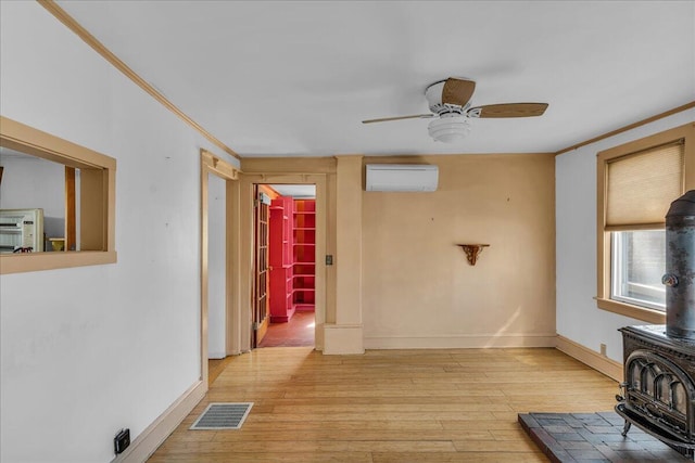 unfurnished living room featuring a wood stove, a ceiling fan, a wall mounted air conditioner, light wood-style flooring, and ornamental molding
