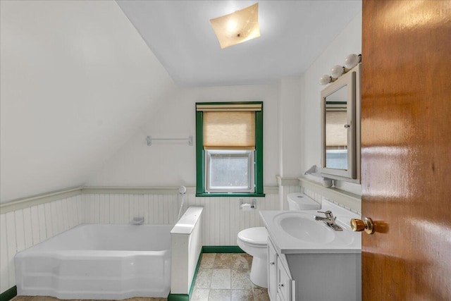 full bathroom with toilet, lofted ceiling, a garden tub, a wainscoted wall, and vanity