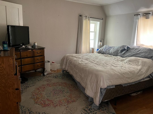 bedroom with wood finished floors, ornamental molding, and vaulted ceiling