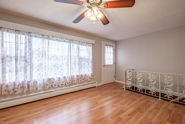 unfurnished room with a baseboard heating unit, wood finished floors, ceiling fan, and a textured ceiling