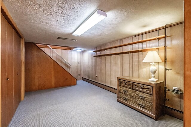 finished basement with a textured ceiling, a baseboard radiator, carpet flooring, and wooden walls