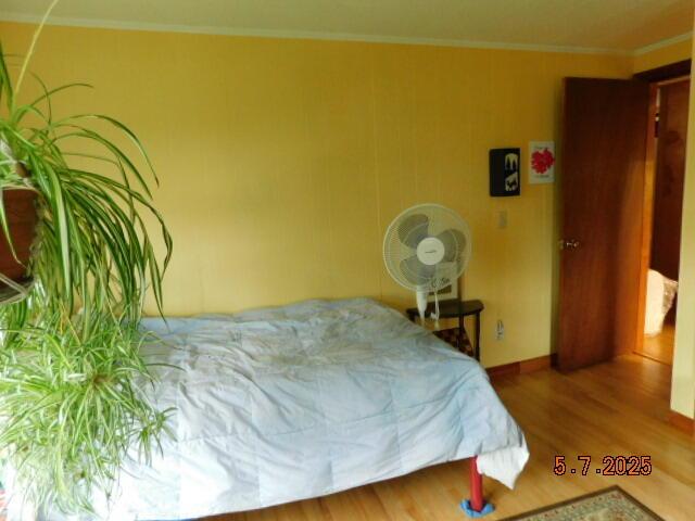 bedroom featuring wood finished floors, crown molding, and baseboards