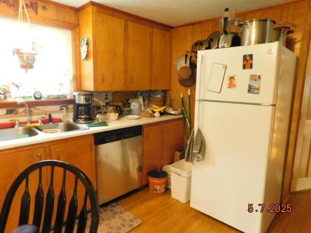 kitchen featuring stainless steel dishwasher, freestanding refrigerator, a sink, light countertops, and light wood-style floors