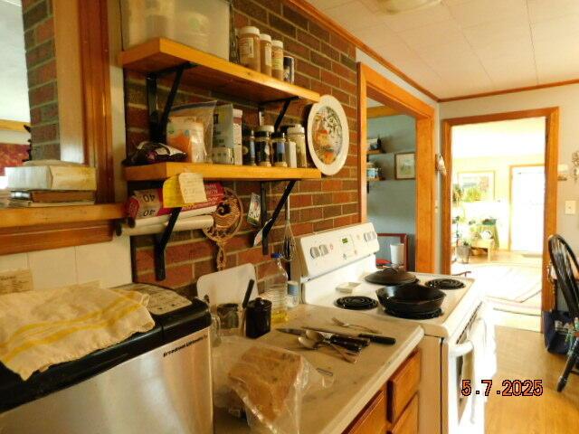 kitchen with white electric range oven, refrigerator, crown molding, and brick wall