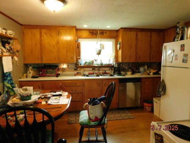kitchen with freestanding refrigerator, stainless steel dishwasher, a sink, light wood-style flooring, and light countertops