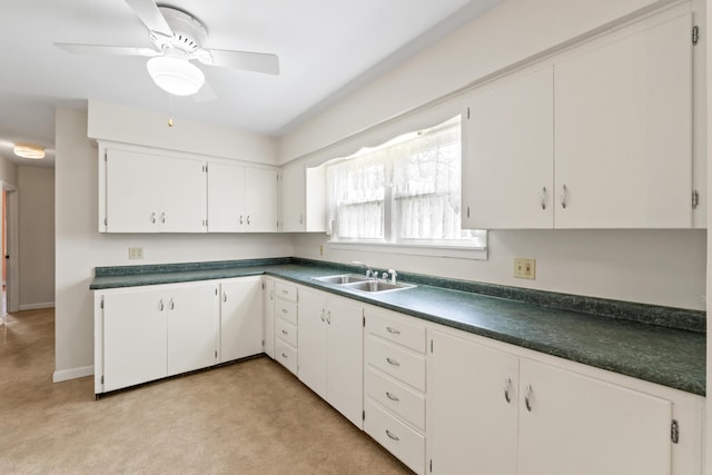 kitchen with a sink, dark countertops, light colored carpet, and white cabinets