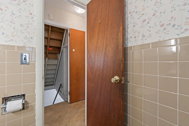 hallway featuring wallpapered walls, tile walls, wainscoting, carpet floors, and stairway