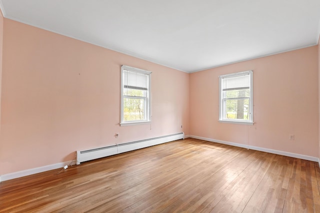 empty room with baseboard heating, light wood finished floors, and baseboards