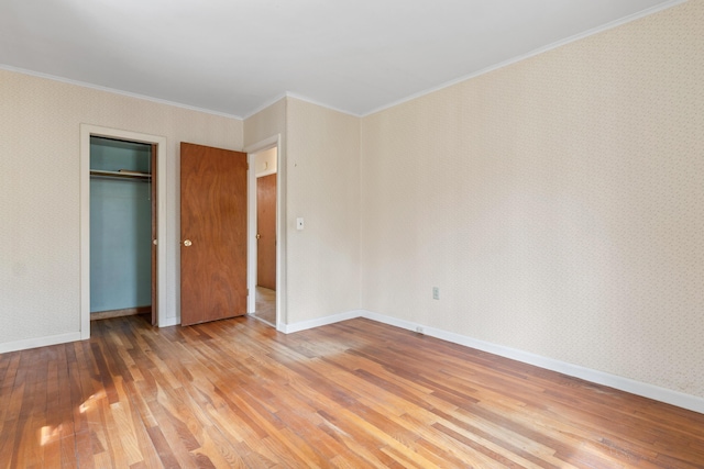 unfurnished bedroom with wood finished floors, crown molding, wallpapered walls, a closet, and baseboards
