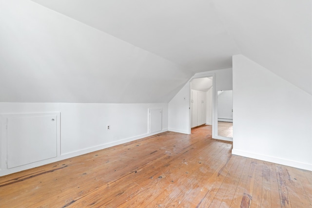 bonus room with vaulted ceiling, light wood-type flooring, baseboards, and a baseboard heating unit