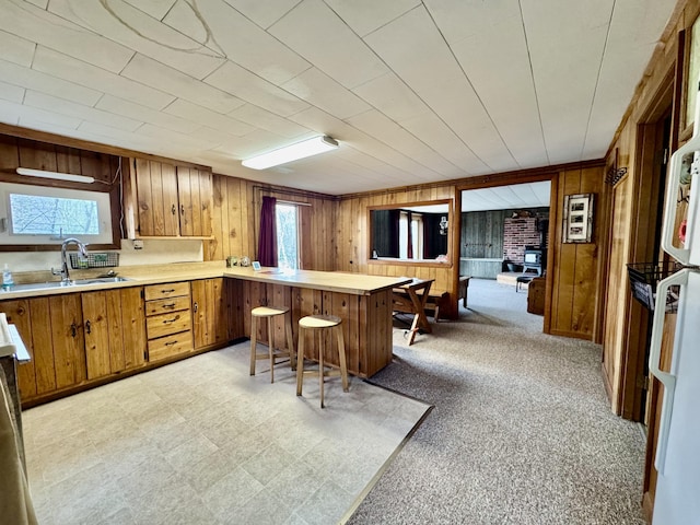 1429 Canada Rd, Moscow, ME 04920 - kitchen featuring a peninsula, wooden walls, brown cabinetry, light countertops, and a breakfast bar