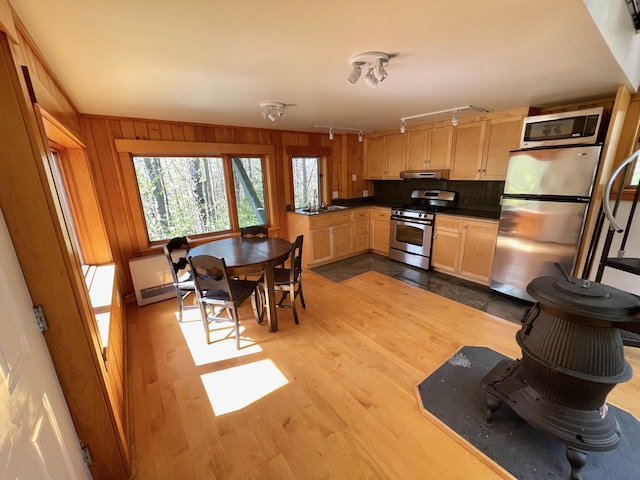 kitchen with stainless steel appliances, under cabinet range hood, light brown cabinetry, wood finished floors, and dark countertops