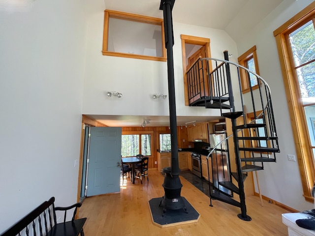 stairway featuring a high ceiling, wood finished floors, baseboards, and a wood stove