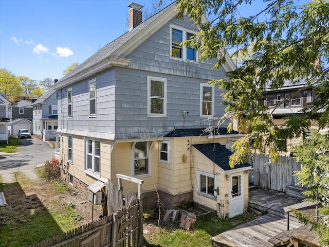 rear view of property featuring a chimney, fence, and roof with shingles