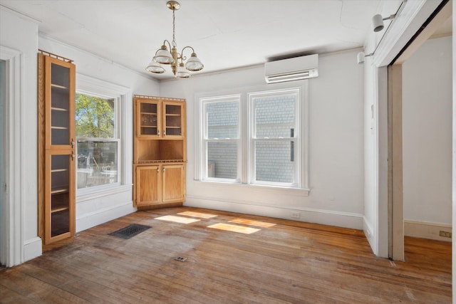 unfurnished dining area with a wall unit AC, wood finished floors, a chandelier, and baseboards