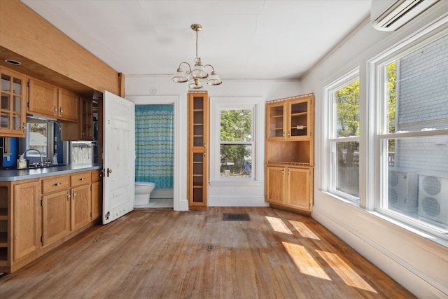 unfurnished dining area featuring a wall mounted AC, light wood-type flooring, a chandelier, and plenty of natural light