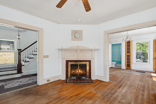 living area with hardwood / wood-style flooring, stairs, a ceiling fan, a chandelier, and a lit fireplace