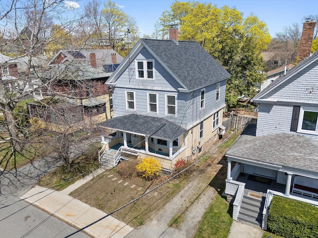 view of front facade with a porch, a chimney, roof with shingles, and fence