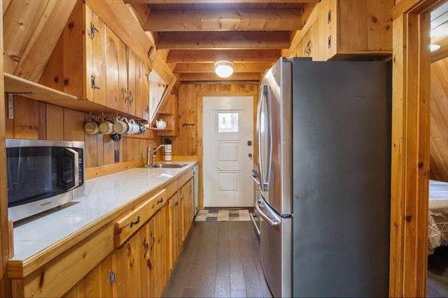 kitchen featuring stainless steel appliances, tile counters, a sink, dark wood-type flooring, and wood walls