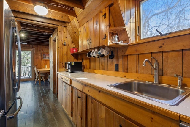 kitchen with tile counters, appliances with stainless steel finishes, a sink, wood walls, and brown cabinets