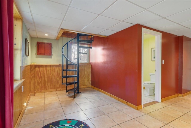 unfurnished room featuring a paneled ceiling, stairs, baseboards, wooden walls, and light tile patterned flooring