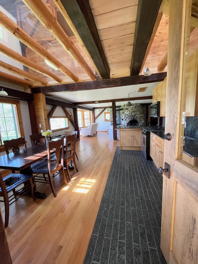 dining area featuring plenty of natural light, a stone fireplace, dark wood-style flooring, and beamed ceiling