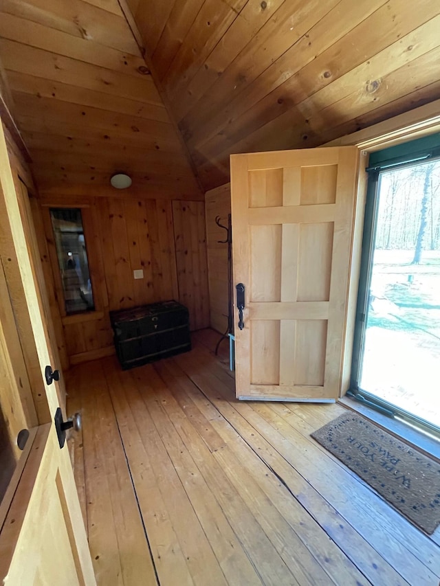 foyer entrance featuring lofted ceiling, wooden ceiling, light wood finished floors, and wood walls