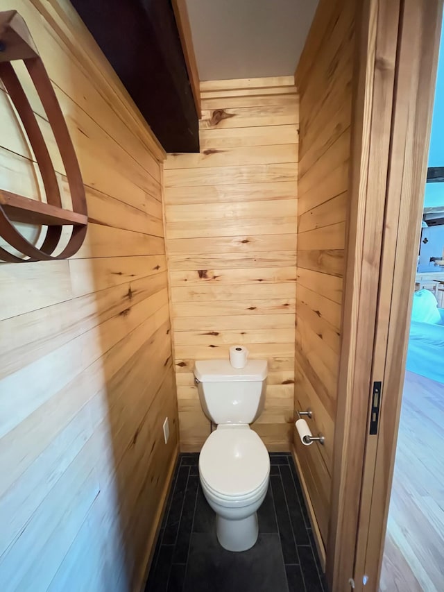 bathroom with wooden walls, toilet, and tile patterned flooring