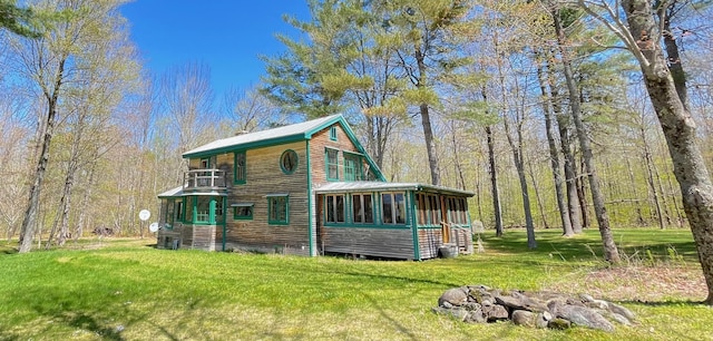 back of house featuring a sunroom, a lawn, a balcony, and a forest view