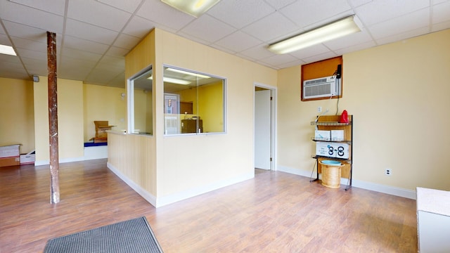 spare room featuring a wall mounted air conditioner, wood finished floors, a drop ceiling, and baseboards