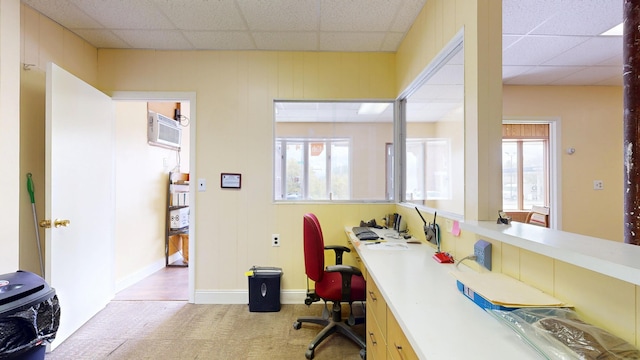 carpeted home office with a drop ceiling, healthy amount of natural light, a wall mounted AC, and baseboards