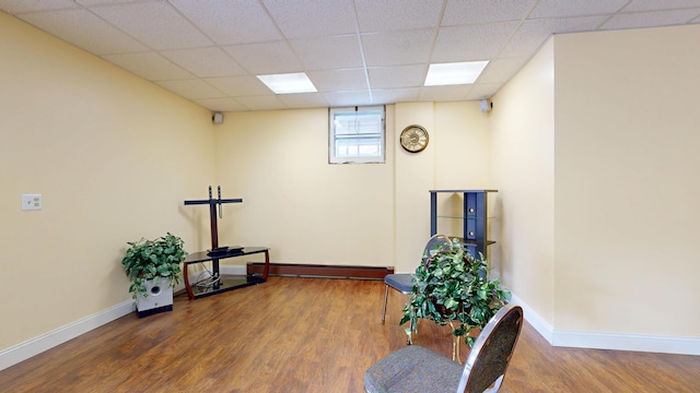 living area featuring a baseboard radiator, wood finished floors, baseboards, and a paneled ceiling