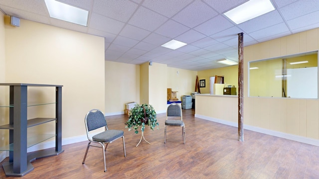 sitting room featuring wood finished floors, a drop ceiling, and baseboards