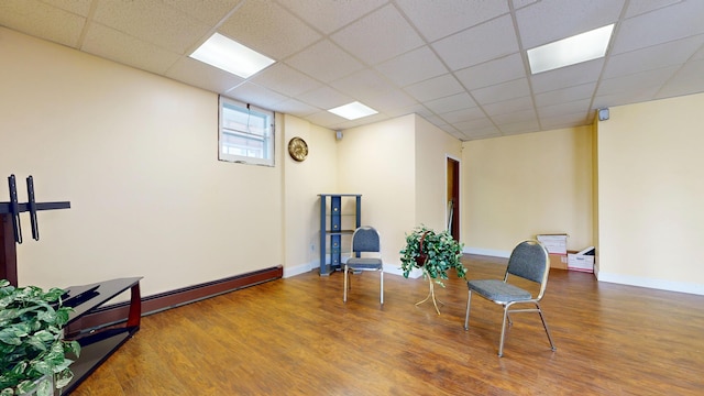 living area with wood finished floors, a paneled ceiling, baseboards, and a baseboard heating unit