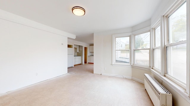 empty room featuring healthy amount of natural light, baseboards, a wall mounted air conditioner, and light floors