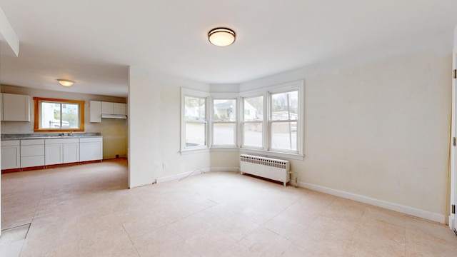 unfurnished dining area with radiator heating unit, a sink, and baseboards