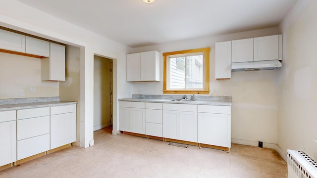 kitchen with under cabinet range hood, radiator, white cabinetry, and light countertops