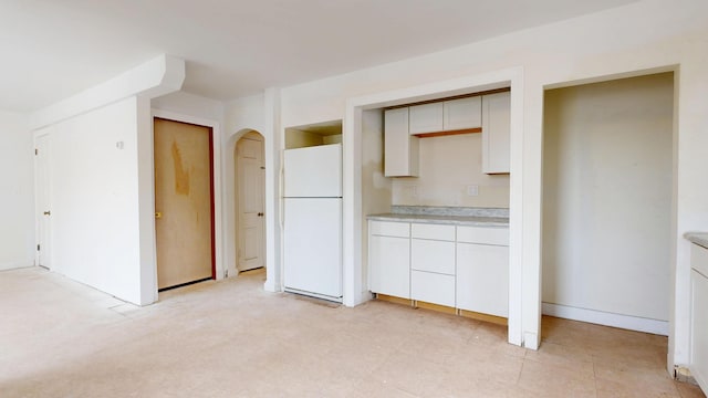 kitchen with freestanding refrigerator, light countertops, arched walkways, and white cabinetry