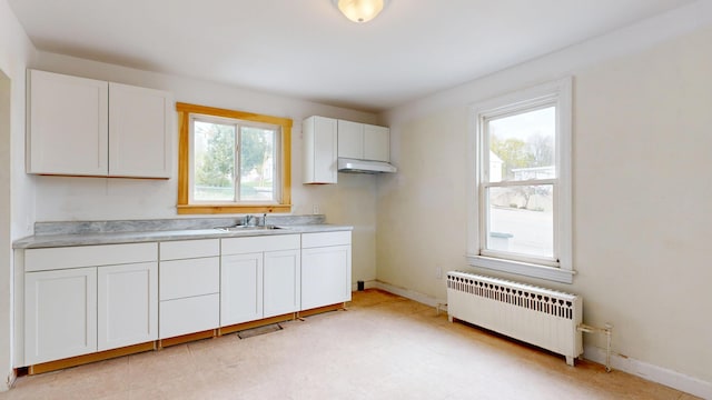 kitchen featuring radiator, a sink, white cabinets, light countertops, and baseboards