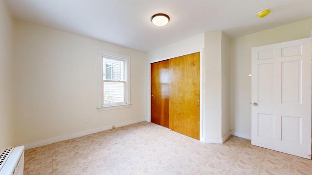 unfurnished bedroom with radiator heating unit, a closet, and baseboards