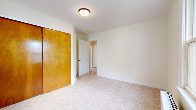 unfurnished bedroom featuring light floors, a closet, radiator, and multiple windows