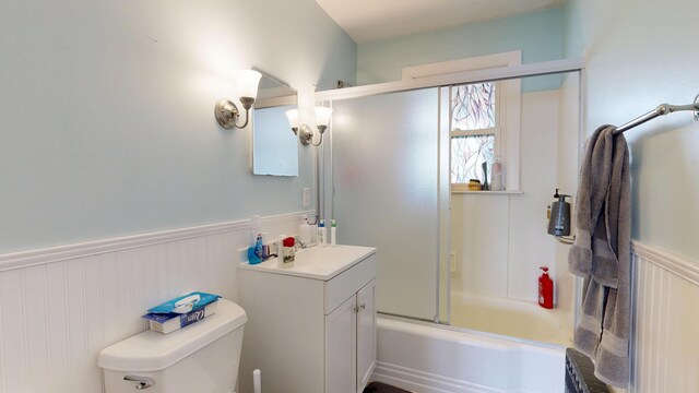 bathroom featuring wainscoting, toilet, vanity, and shower / bath combination with glass door
